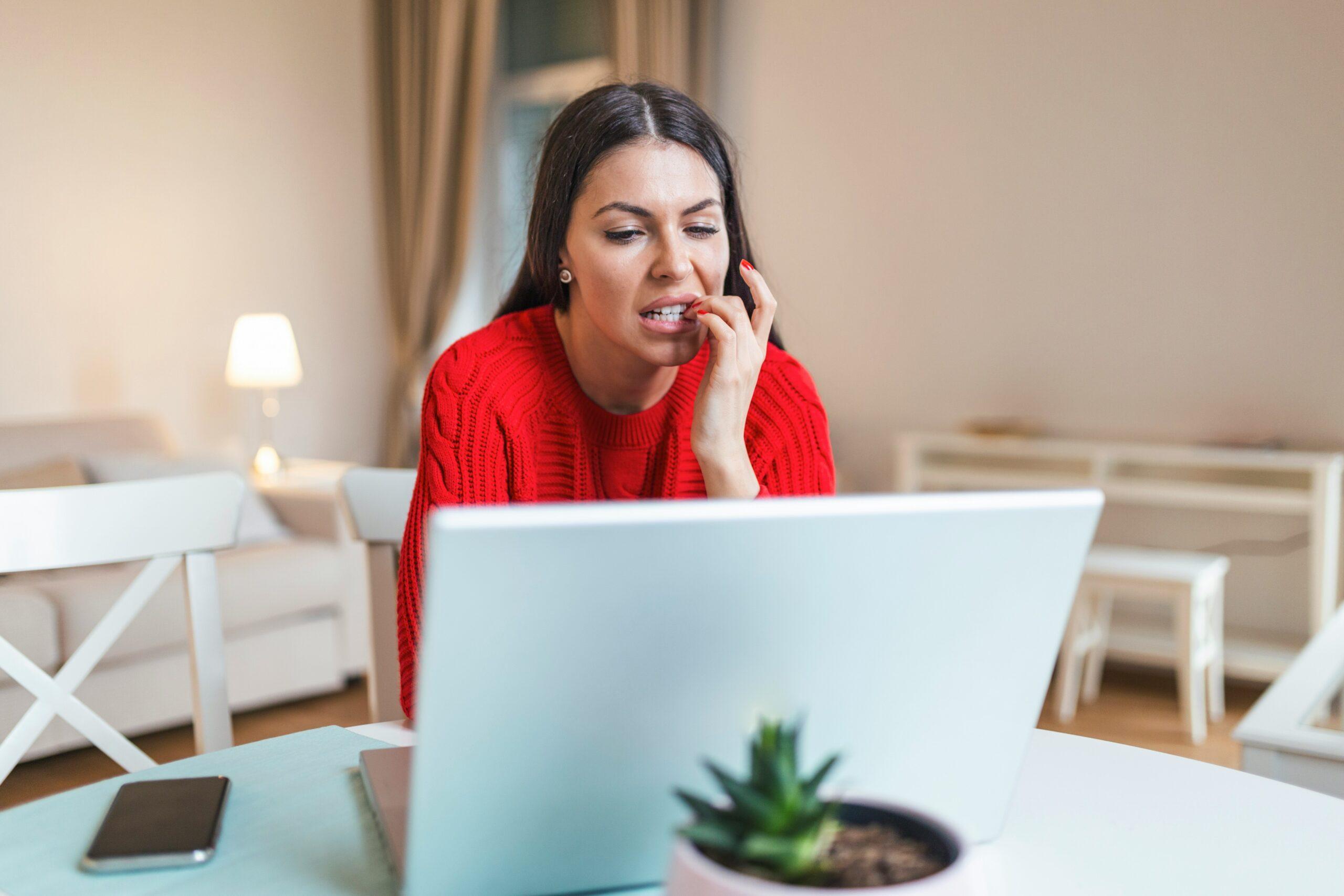 a woman biting her nails while looking at a laptop