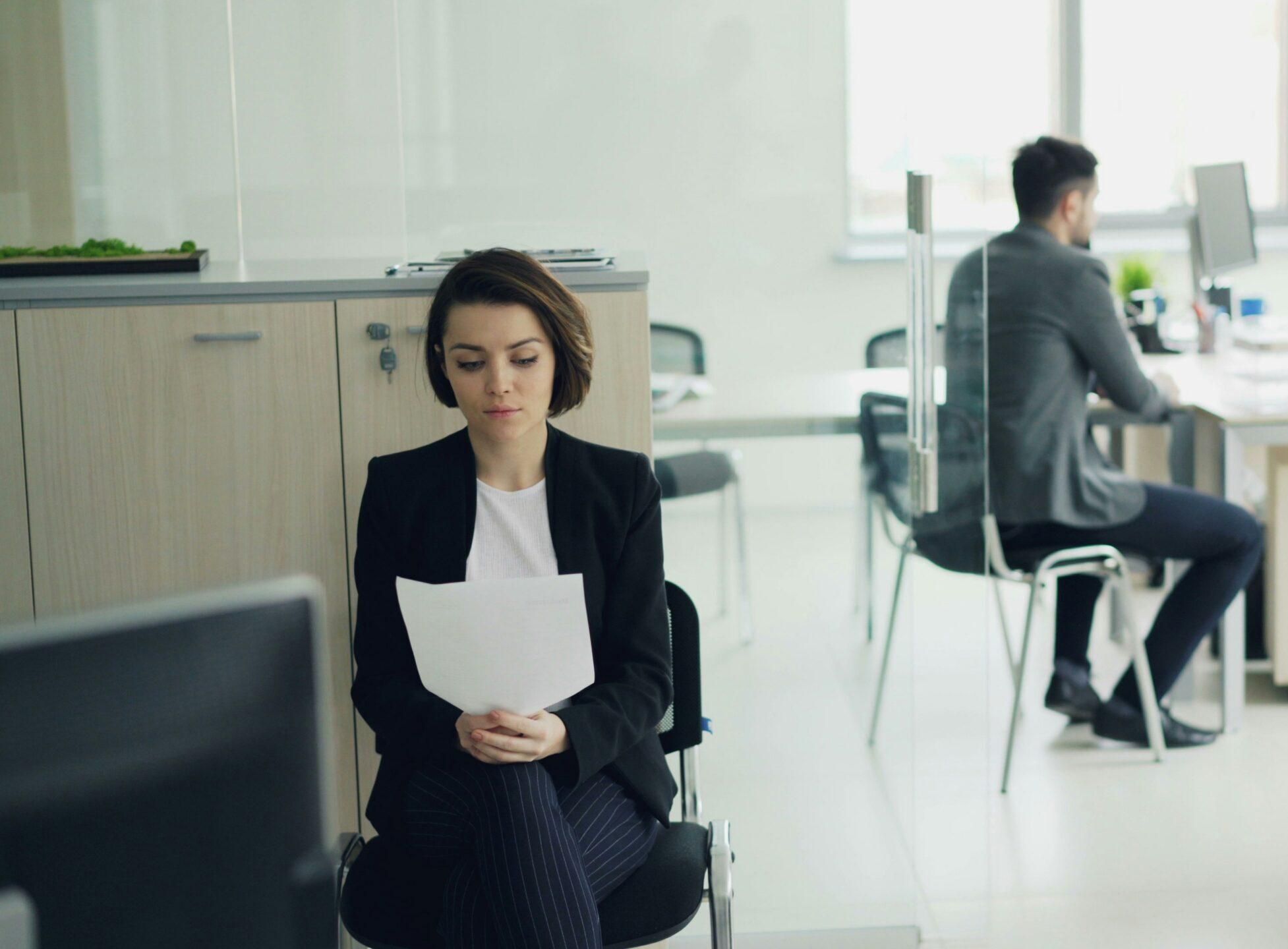 A woman sitting at a desk in an office surrounded by colleagues engaged in discussion.